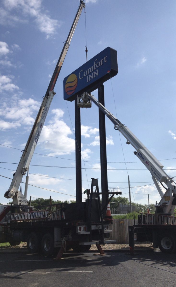 A tall and colorful sign being installed outside a hotel, representing how one can benefit from calling a commercial sing company in Tinley Park.