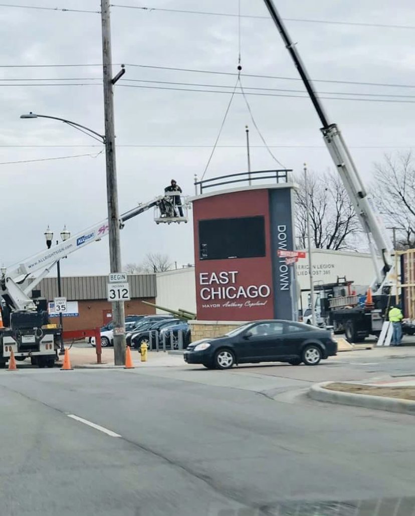 A brown and gray sign being setup outside of a busy intersection, representing how one can benefit from calling a Joliet commercial sign company.