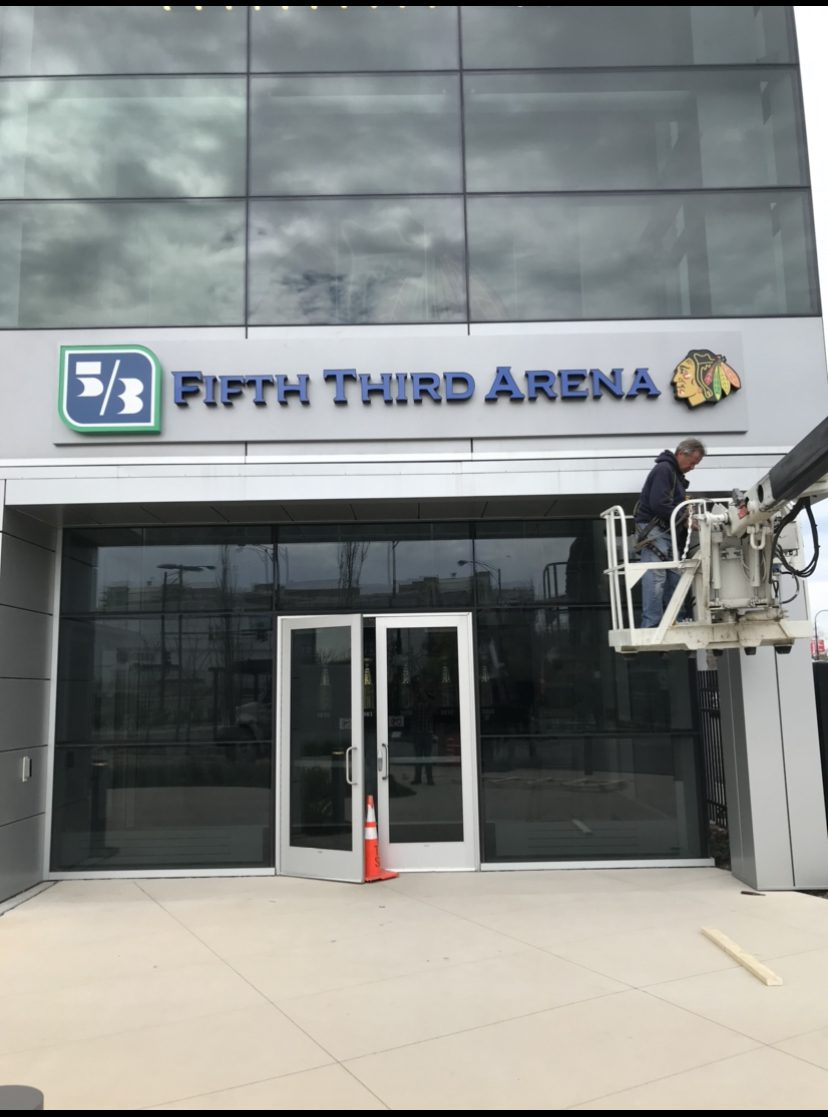 The outside of a bank and a man is working on their sign that says "5/3 Fifth Third Arena", representing how one can benefit from calling the best commercial sign company in Chicago.