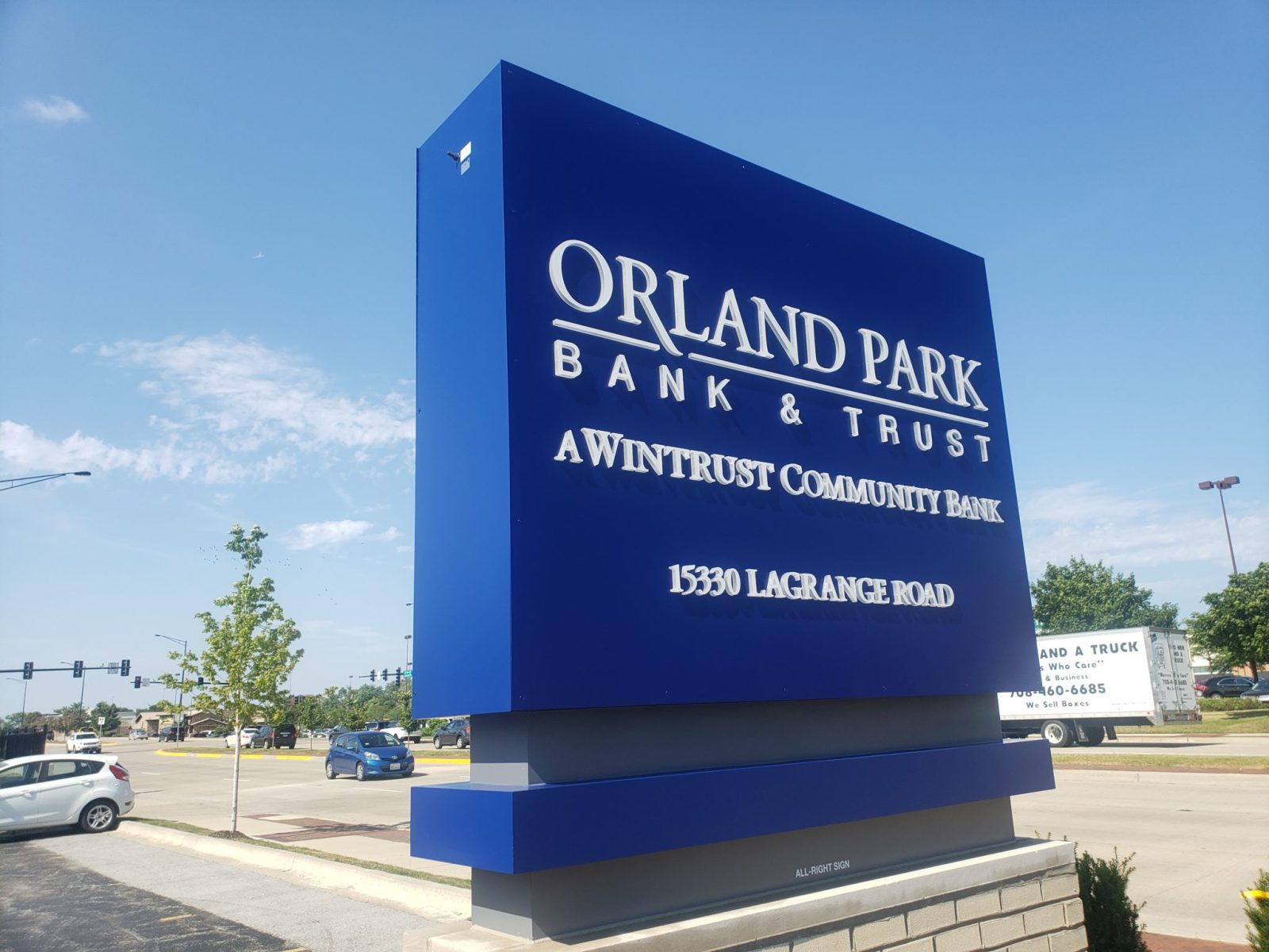 A busy intersection with a blue sign outside a building that says "Orland Park Bank & Trust", representing how one can benefit from calling a Joliet monument sign company.